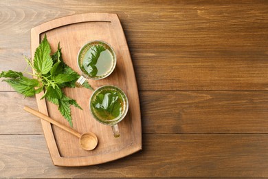 Glass cups of aromatic nettle tea and green leaves on wooden table, top view. Space for text