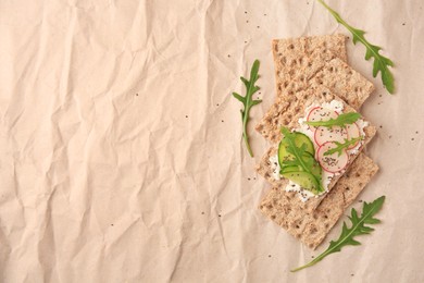 Tasty crispbreads with cream cheese, fresh cucumbers, radish and arugula on parchment paper, flat lay. Space for text