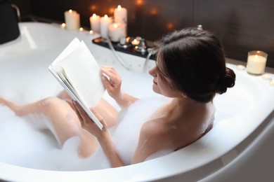 Photo of Young woman reading book while taking bubble bath. Romantic atmosphere