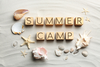 Flat lay composition with phrase SUMMER CAMP made of wooden cubes on sand