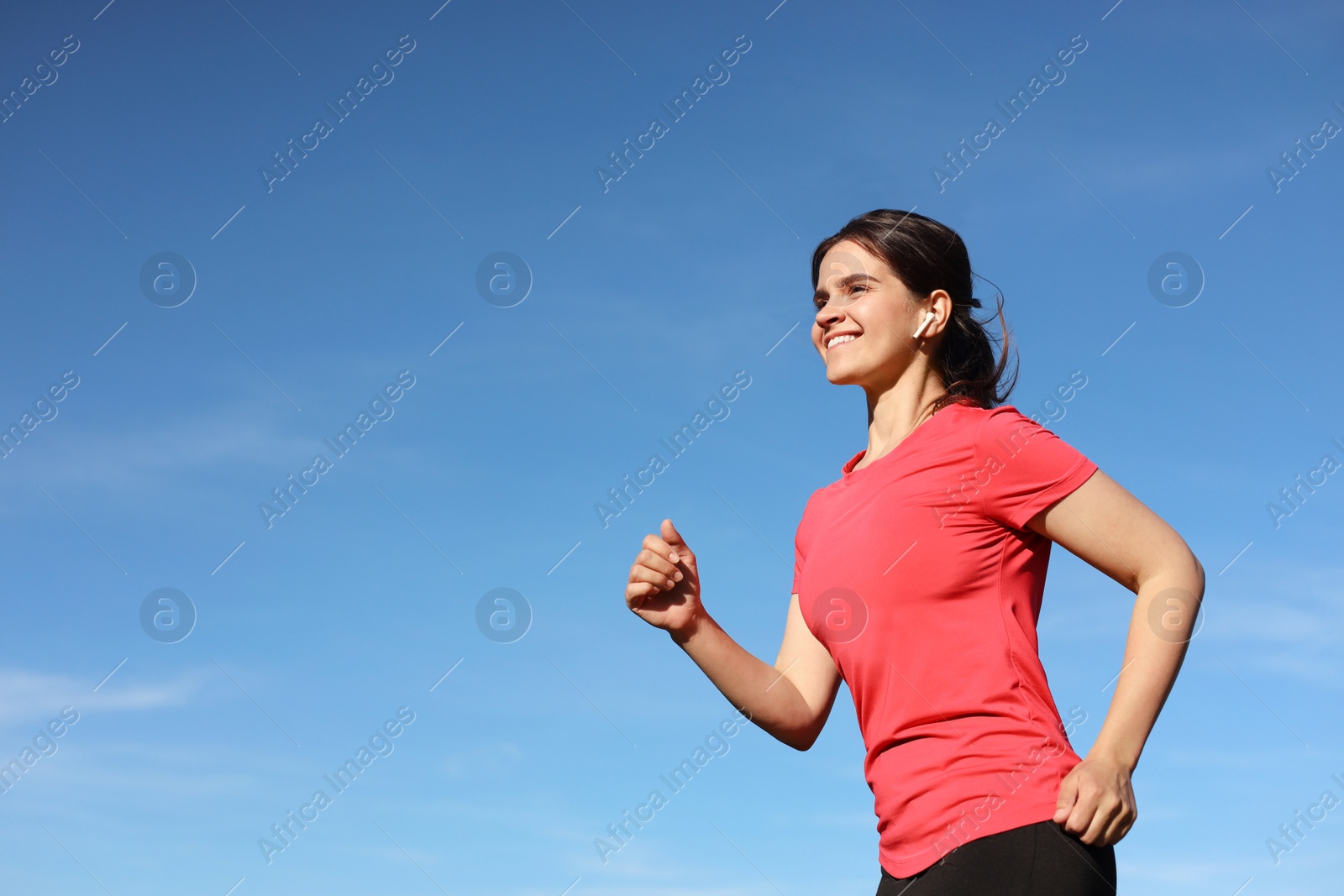 Photo of Young woman listening to music while running outdoors in morning, low angle view. Space for text