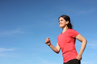 Young woman listening to music while running outdoors in morning, low angle view. Space for text