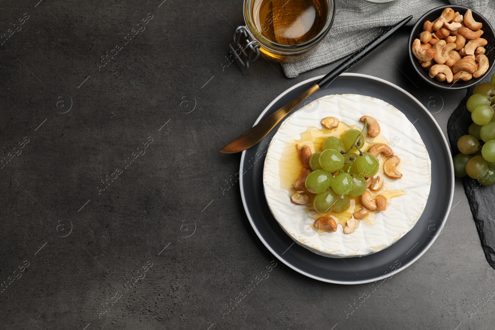 Photo of Brie cheese served with grape, cashew nuts and honey on dark grey table, flat lay. Space for text