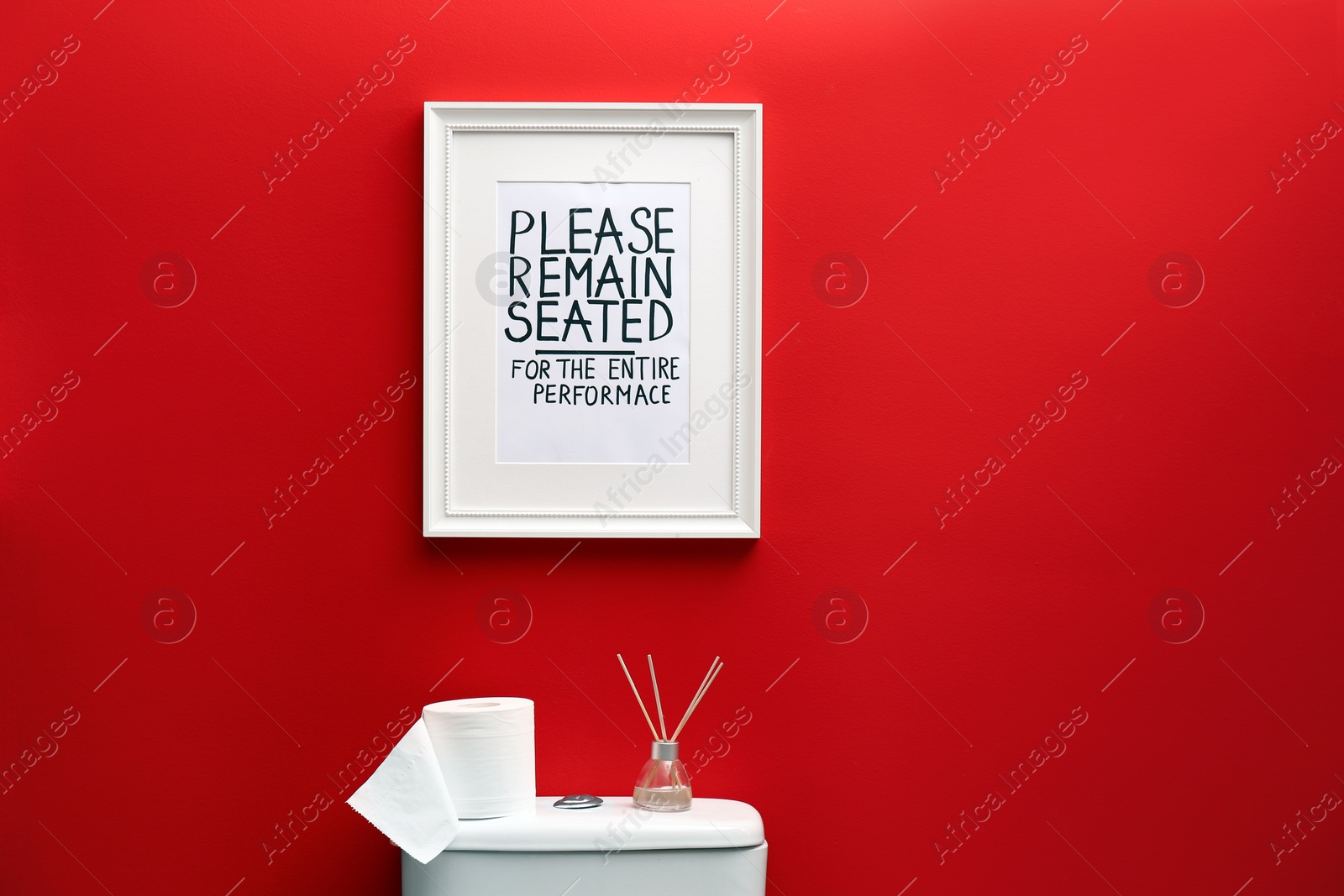 Photo of Toilet bowl and funny sign near red wall. Bathroom interior