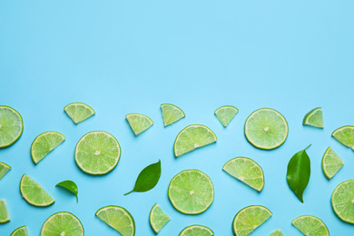 Photo of Juicy fresh lime slices and green leaves on light blue background, flat lay. Space for text