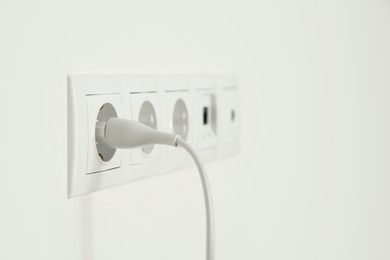 Many power sockets with plug on white wall indoors. Space for text