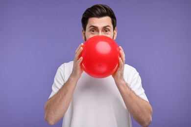 Man inflating red balloon on purple background