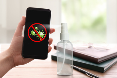 Image of Sanitizing mobile devices during coronavirus outbreak. Antiseptic spray and woman with smartphone indoors, closeup