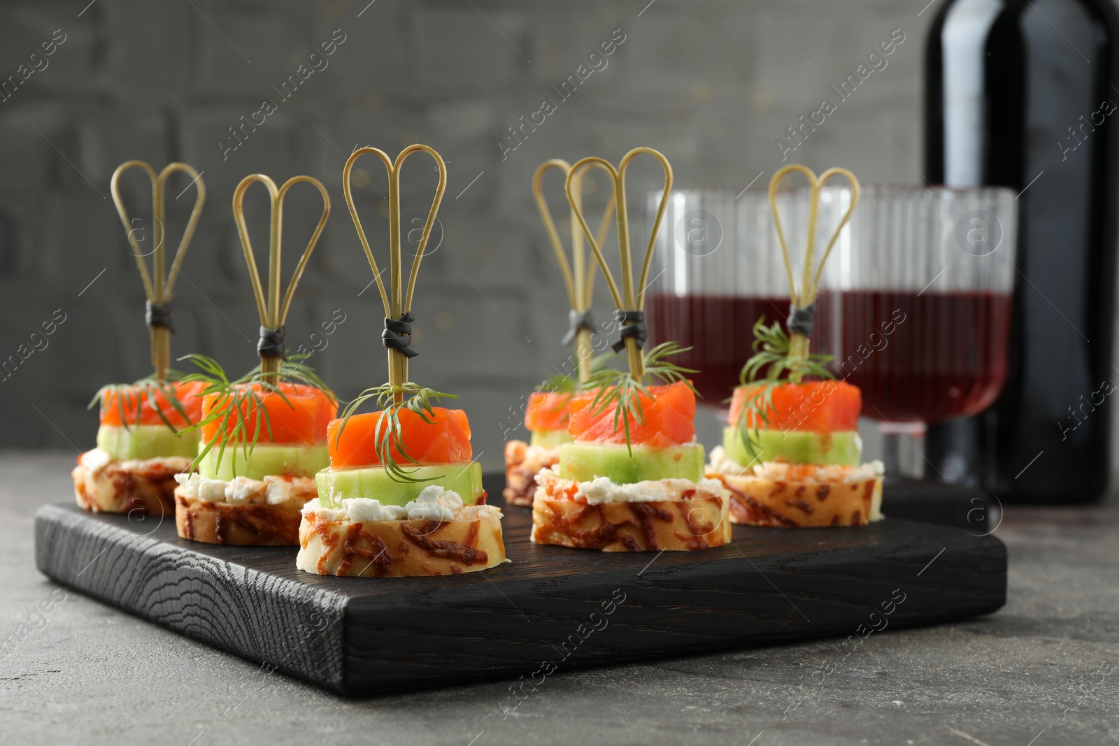 Photo of Tasty canapes with salmon, cucumber, bread and cream cheese served on grey table, closeup