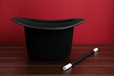 Photo of Black top hat and wand on wooden table. Magician equipment