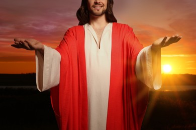 Image of Jesus Christ with outstretched arms outdoors at sunset