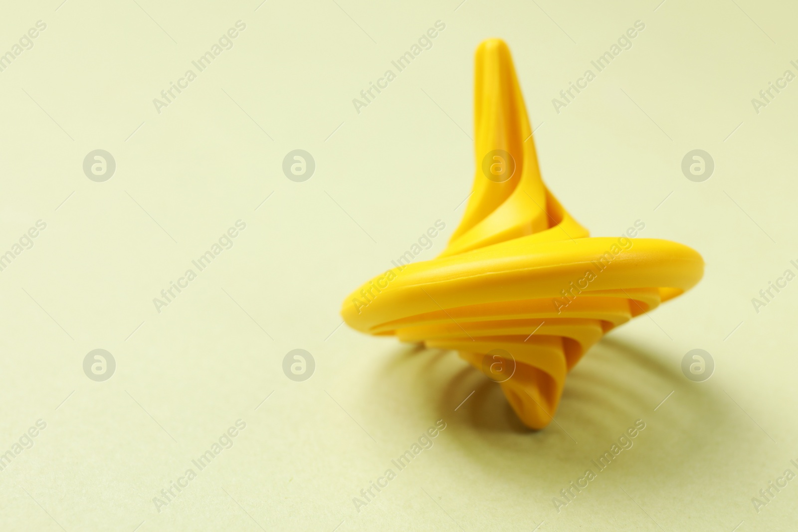 Photo of One yellow spinning top on green background, closeup. Space for text