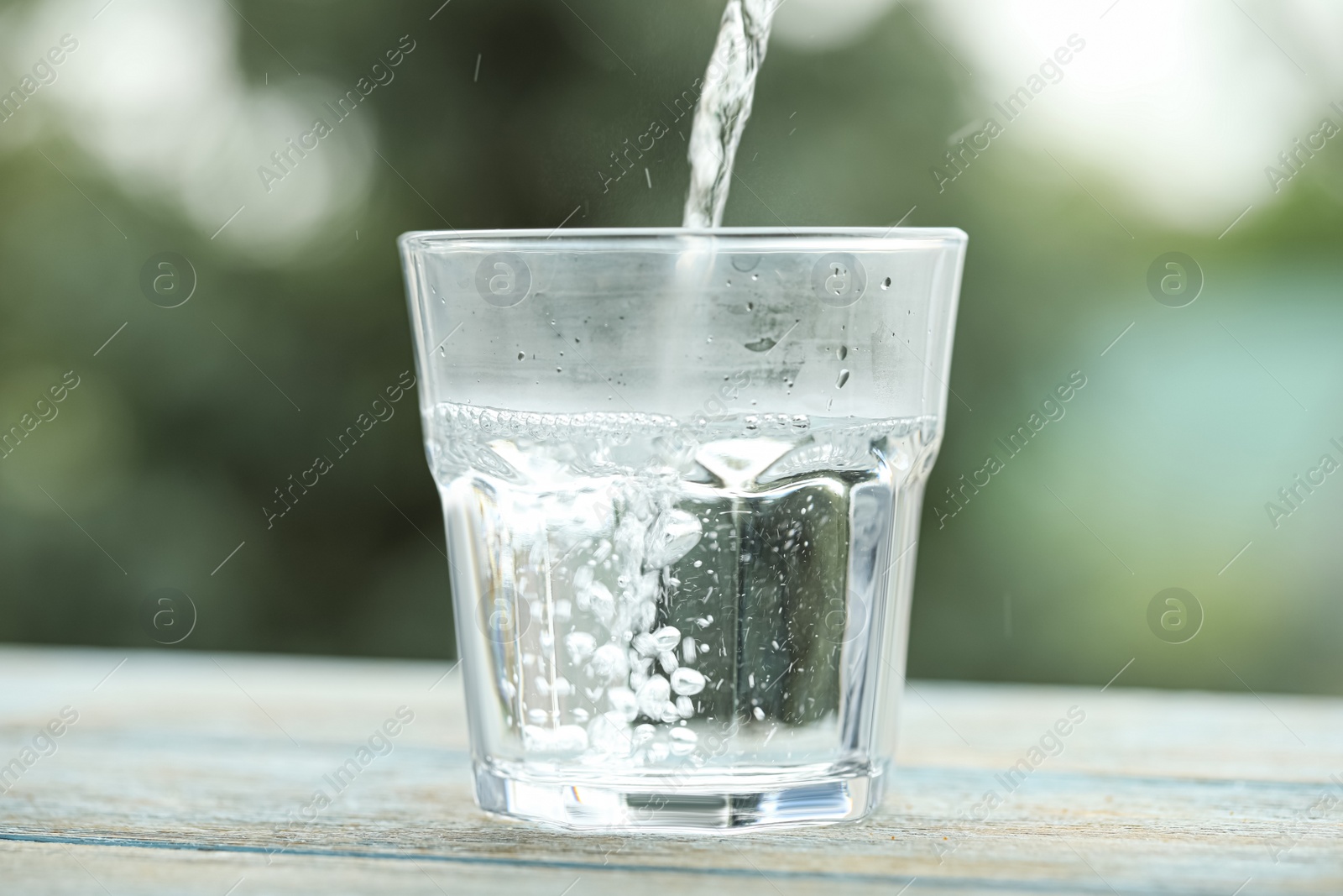 Photo of Pouring pure water into glass on light blue wooden table against blurred background