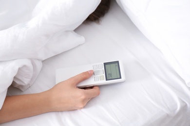 Photo of Woman holding air conditioner remote control in bed, focus on hand