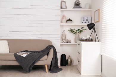 Photo of Stylish living room interior with comfortable sofa, wall shelves and beautiful decor elements