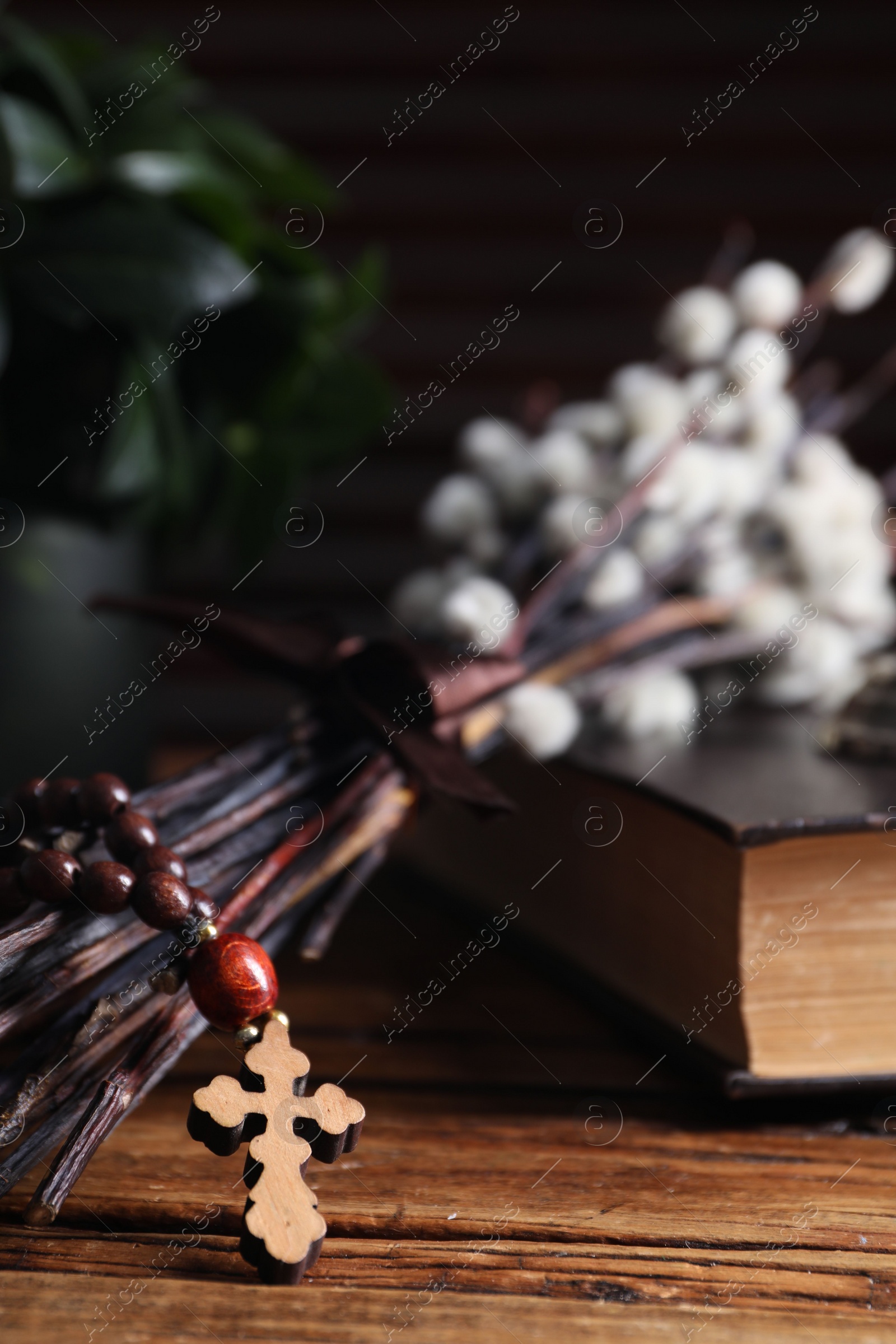 Photo of Rosary beads, Bible and willow branches on wooden table, closeup