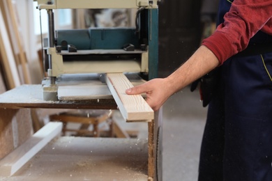 Photo of Working man using thickness planer at carpentry shop, closeup