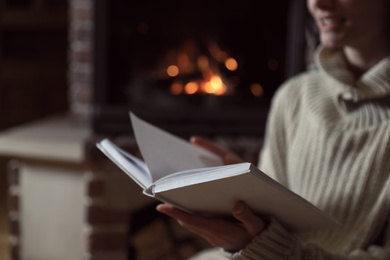 Woman reading book near burning fireplace at home, closeup