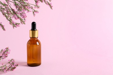 Photo of Bottle with cosmetic oil and flowers on pink background, space for text