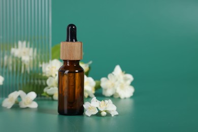 Photo of Essential oil in bottle and beautiful jasmine flowers on green background, space for text