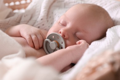 Photo of Cute newborn baby with pacifier sleeping on white blanket, closeup