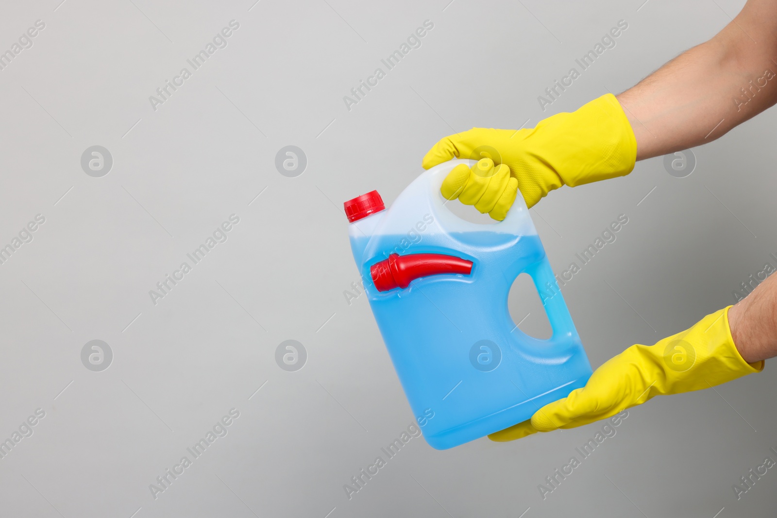 Photo of Man in rubber gloves holding canister with blue liquid on light grey background, closeup. Space for text
