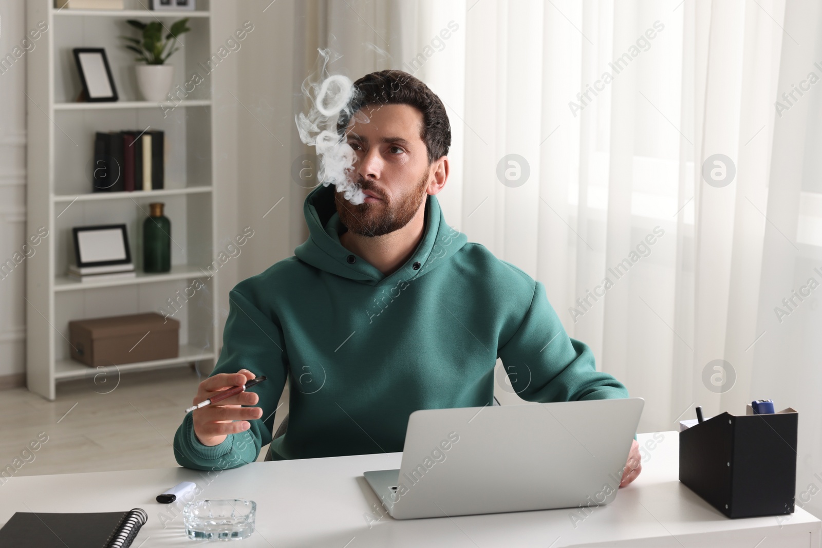 Photo of Man using cigarette holder for smoking at workplace in office