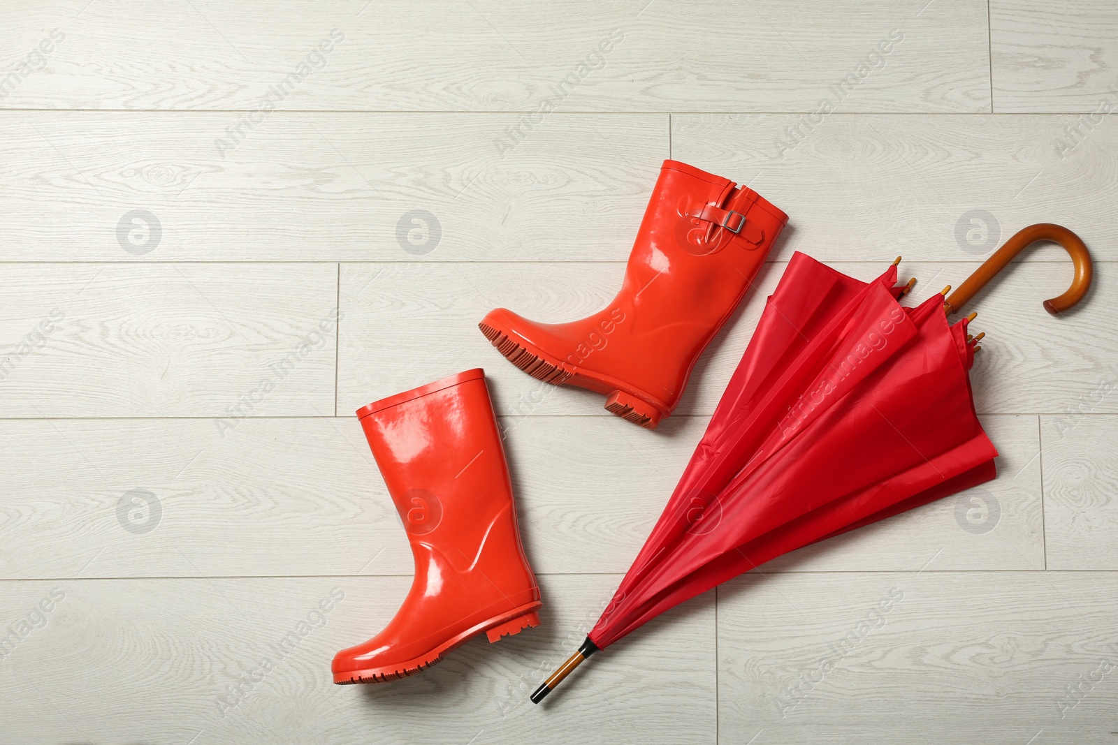 Photo of Color umbrella and rubber boots on wooden floor, flat lay. Space for text