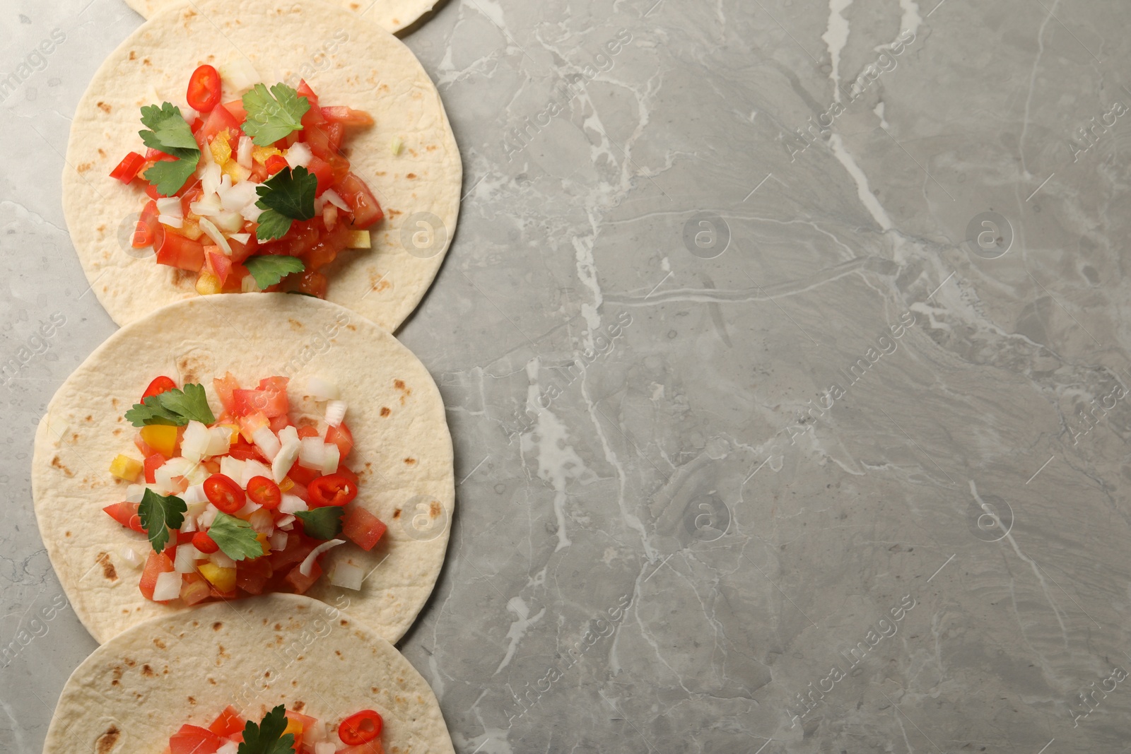 Photo of Delicious tacos with vegetables and parsley on grey marble table, top view. Space for text