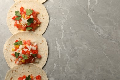 Photo of Delicious tacos with vegetables and parsley on grey marble table, top view. Space for text