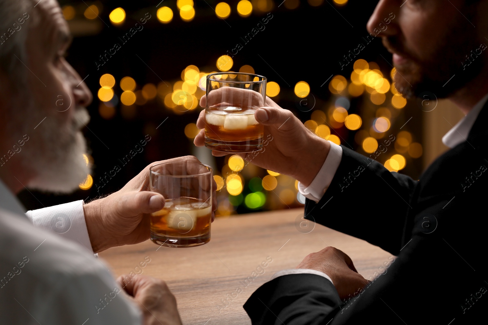 Photo of Men with glasses of whiskey talking at wooden table in bar