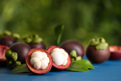 Photo of Delicious ripe mangosteen fruits on blue wooden table outdoors