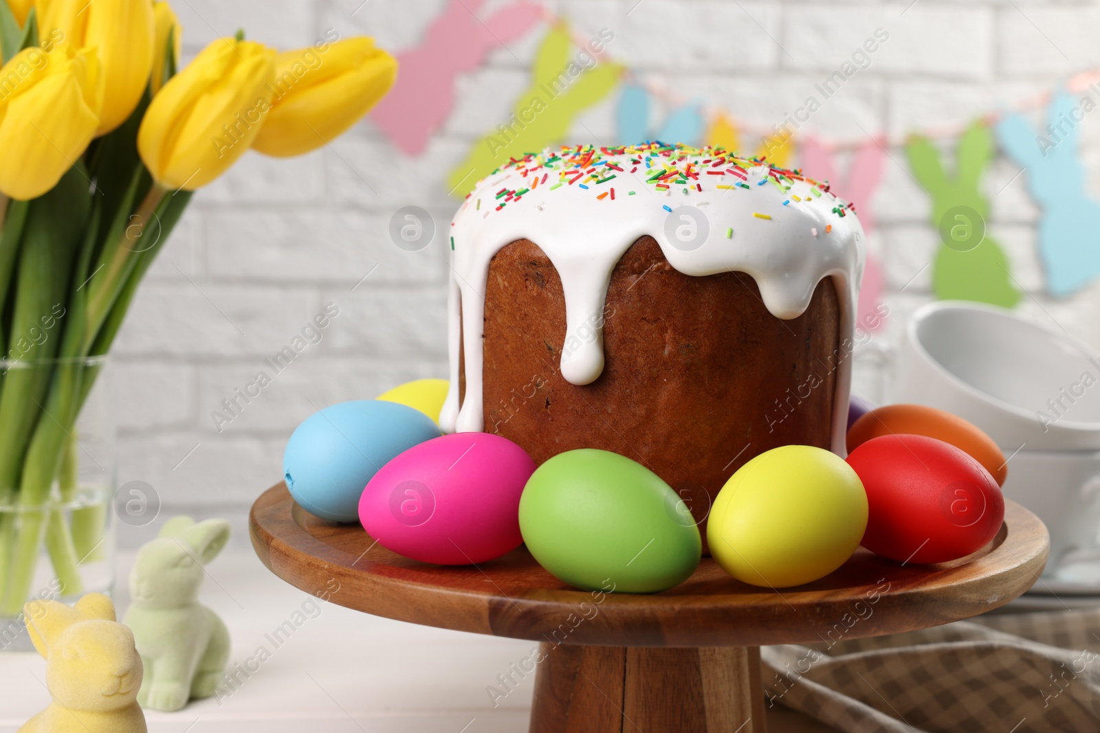 Photo of Stand with tasty Easter cake and decorated eggs on white wooden table