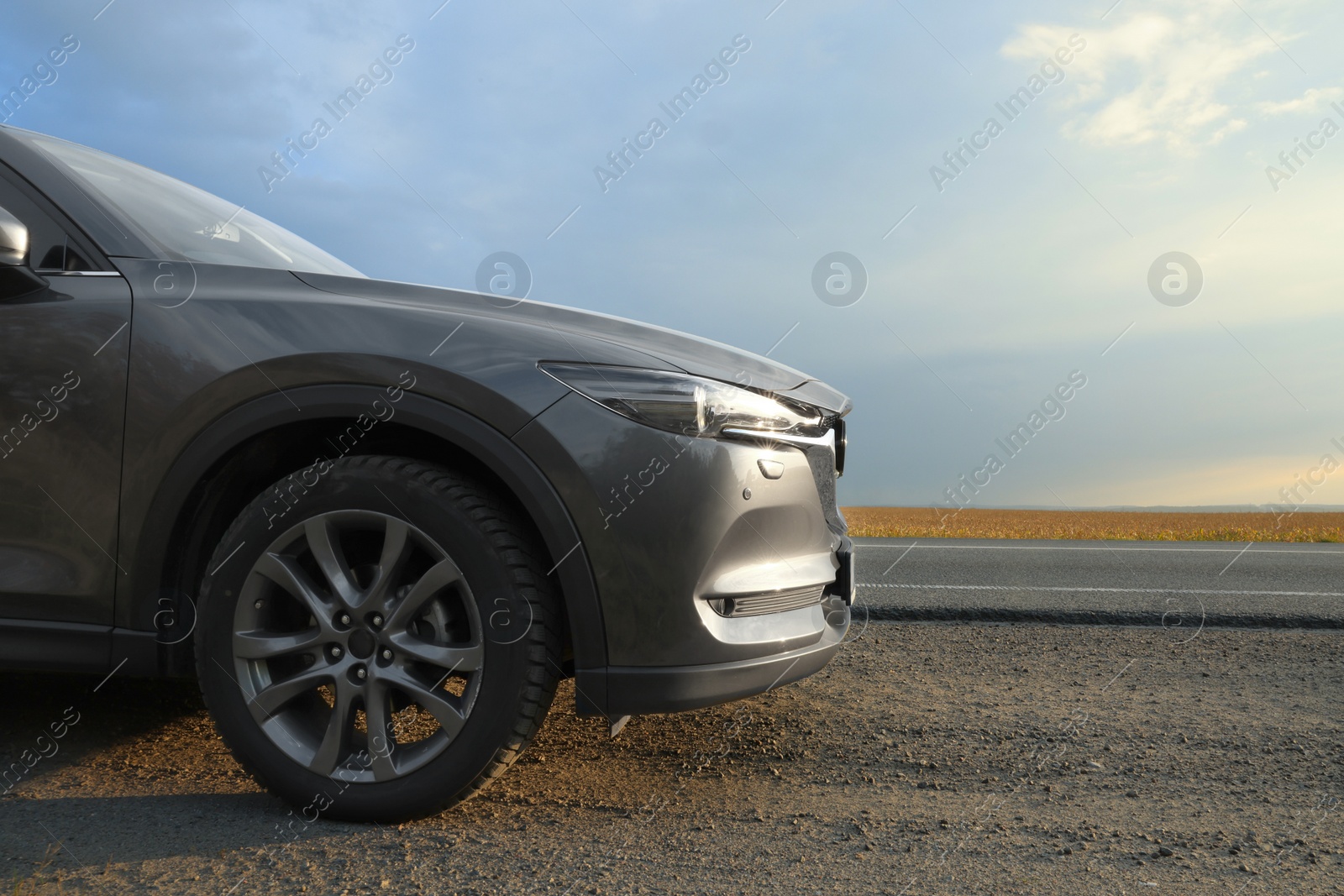 Photo of Black modern car parked on roadside at sunset, closeup. Space for text