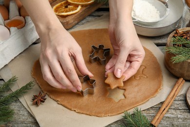 Photo of Woman cutting dough with cookie cutter at wooden table, closeup. Christmas biscuits