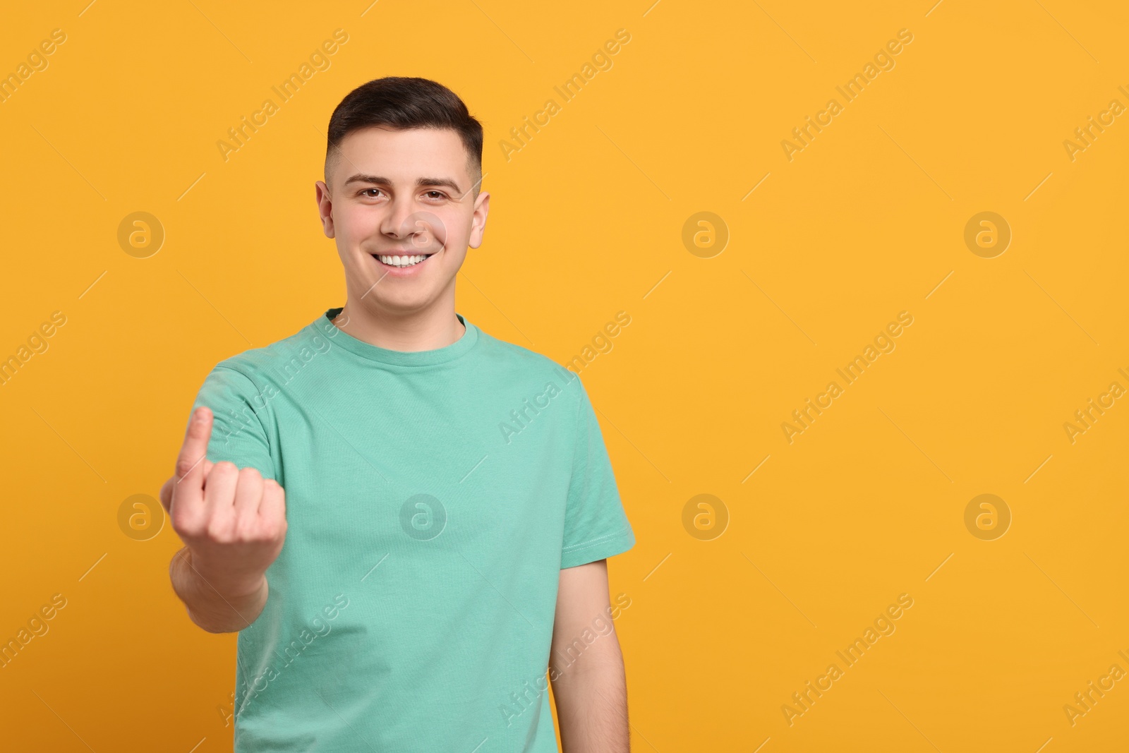 Photo of Handsome man inviting to come in against orange background. Space for text