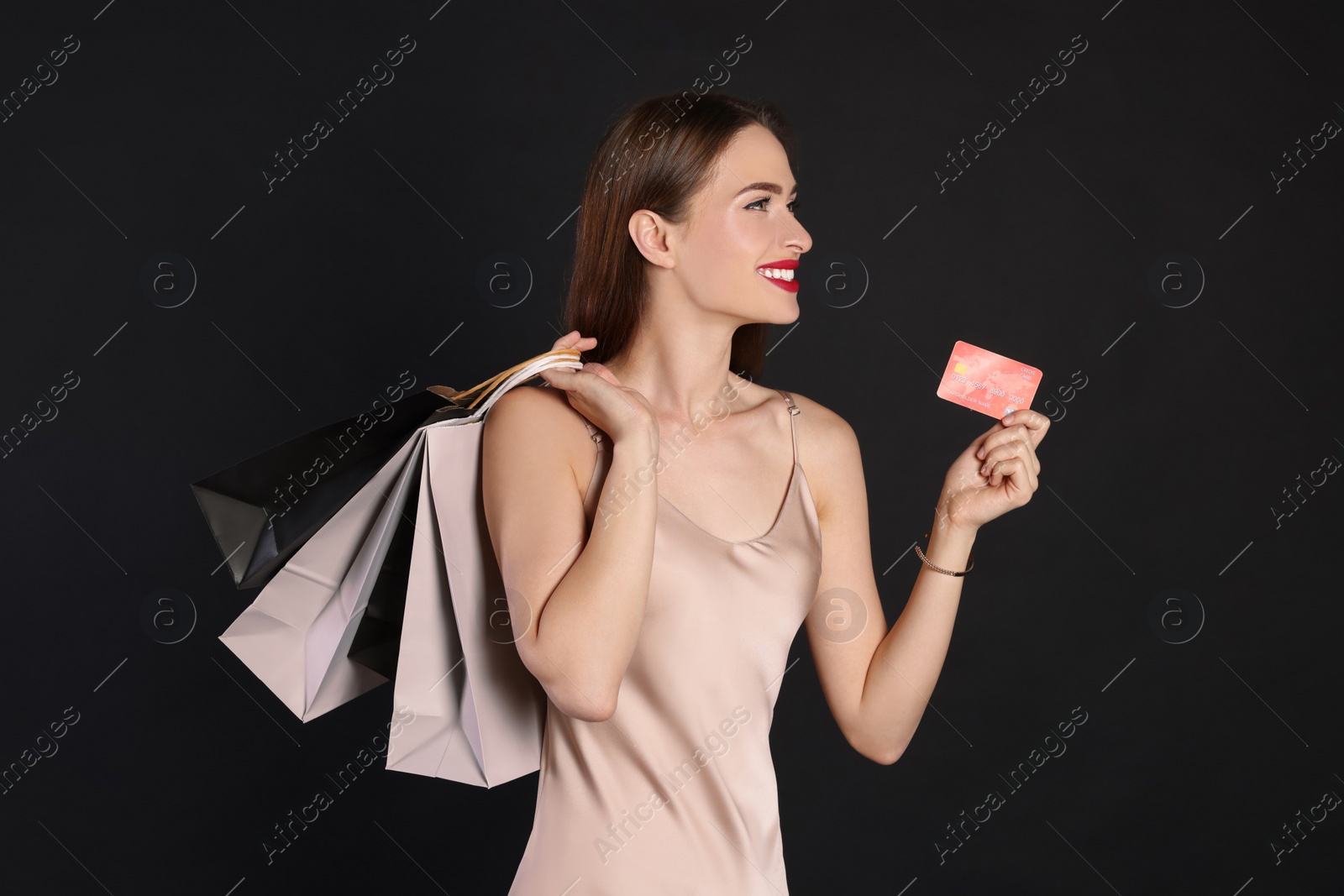 Photo of Happy young woman with shopping bags and credit card on black background. Big sale