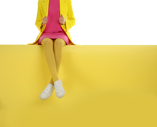 Woman wearing yellow tights and stylish shoes sitting on color background, closeup. Space for text