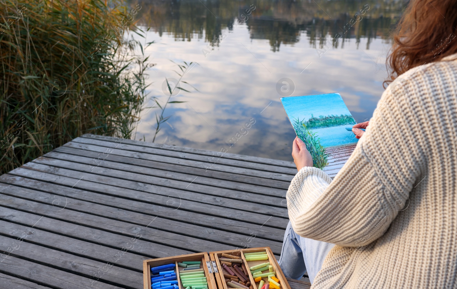 Photo of Woman drawing with soft pastels on wooden pier near river, closeup