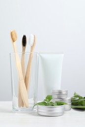 Toothbrushes, dental products and herbs on white wooden table
