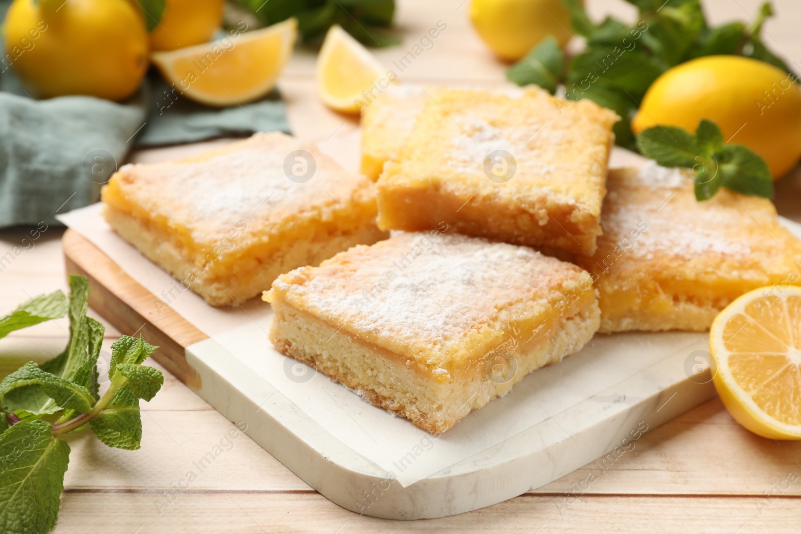 Photo of Tasty lemon bars with powdered sugar and mint on wooden table, closeup