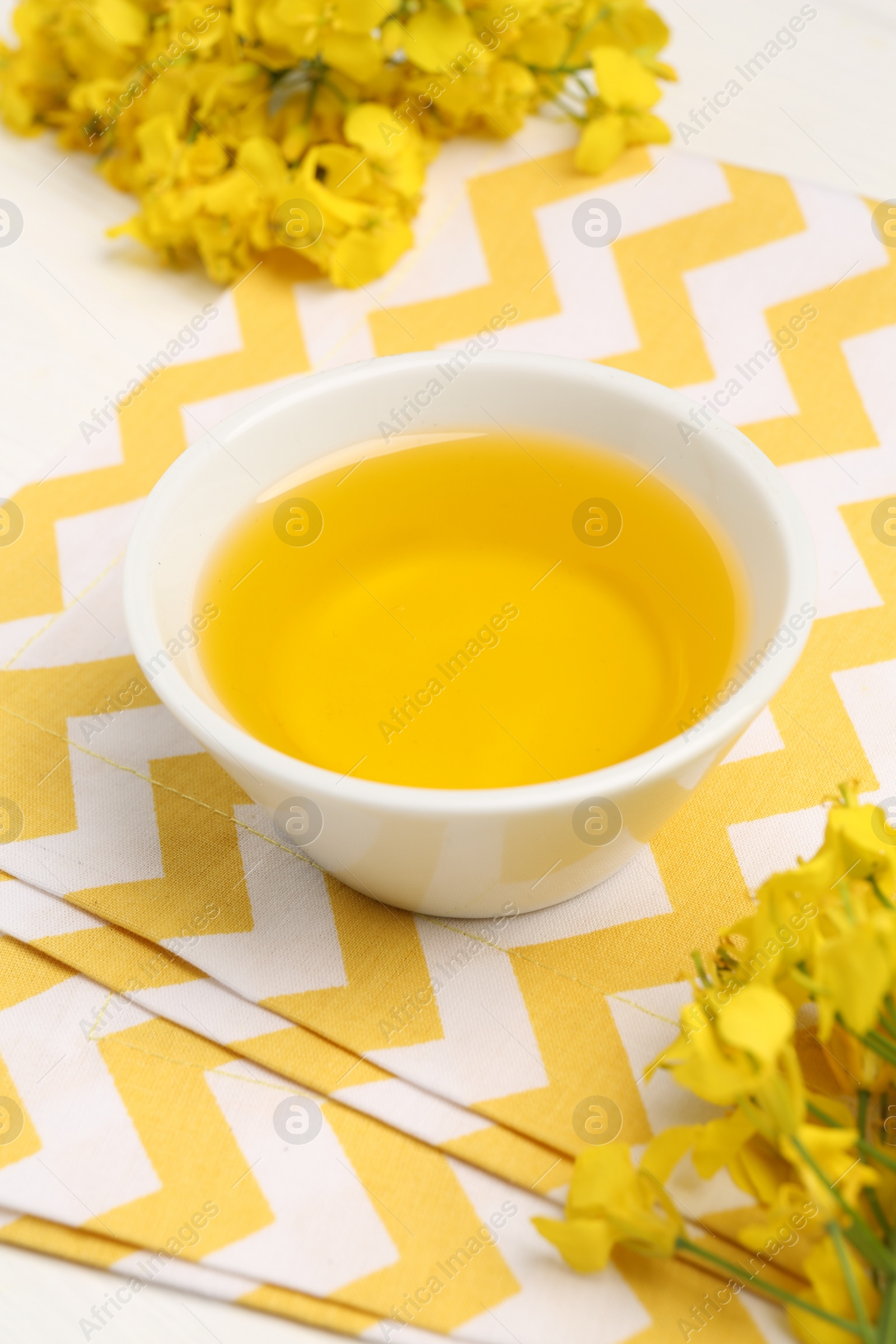 Photo of Rapeseed oil in bowl and beautiful yellow flowers on table