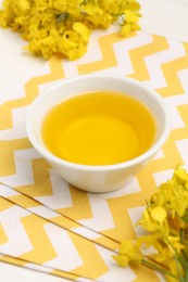 Photo of Rapeseed oil in bowl and beautiful yellow flowers on table