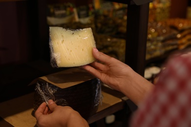 Woman choosing tasty cheese from display in store