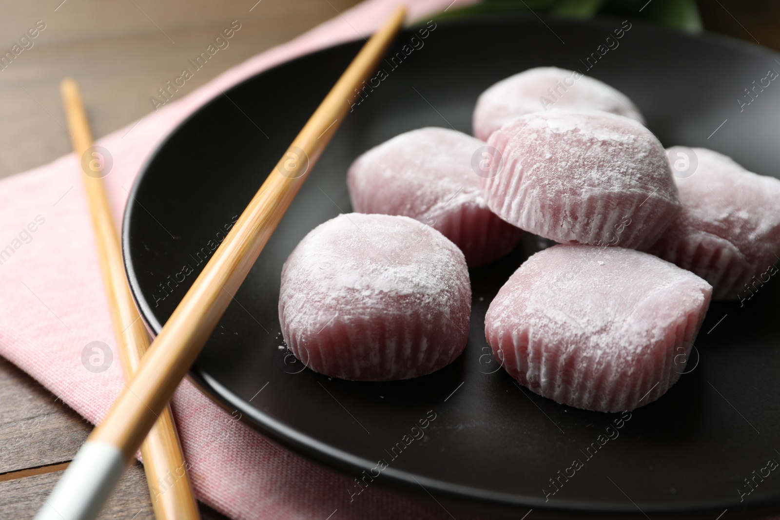 Photo of Black plate with delicious mochi and chopsticks on wooden table, closeup. Traditional Japanese dessert