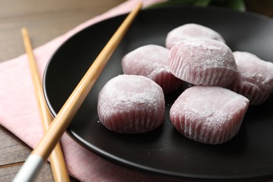 Black plate with delicious mochi and chopsticks on wooden table, closeup. Traditional Japanese dessert