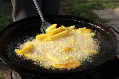 Photo of Cooking delicious potato wedges on frying pan outdoors