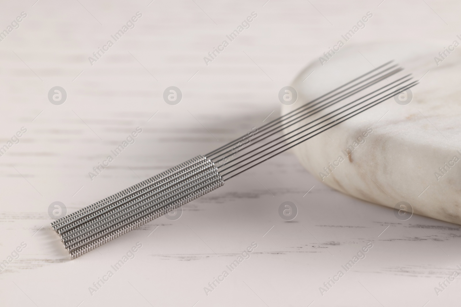 Photo of Acupuncture needles and spa stone on white wooden table, closeup