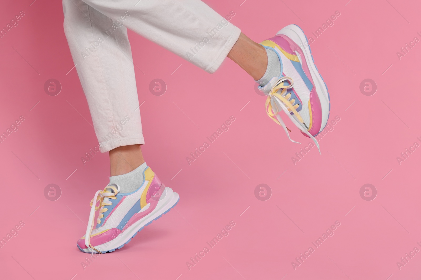 Photo of Woman wearing pair of new stylish sneakers on pink background, closeup