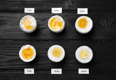Photo of Different cooking time and readiness stages of boiled chicken eggs on black wooden table, flat lay
